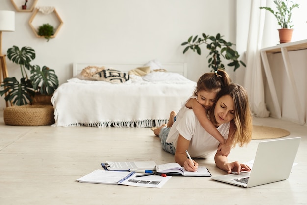 Daughter plays with mom and cat while mom works on computer