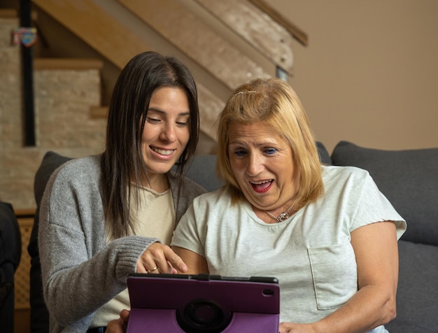 Daughter showing her mother something on the tablet and the mother is surprised while they are happily sitting on the sofa at home