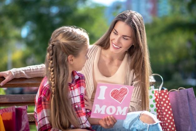 Daughter sitting with her mom on park bench, presenting her card