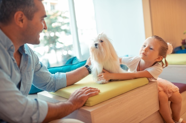 Daughter talking to daddy and touching their white fluffy dog