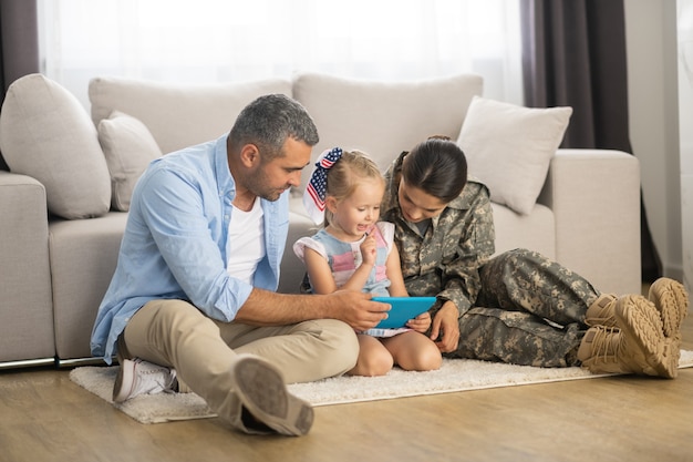 Daughter watching cartoon. Cute blonde daughter watching cartoon near father and mom serving in armed forces