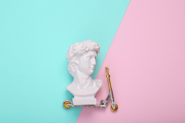 David bust ride on Kick scooter pink blue background Creative layout Minimal still life Flat lay Top view