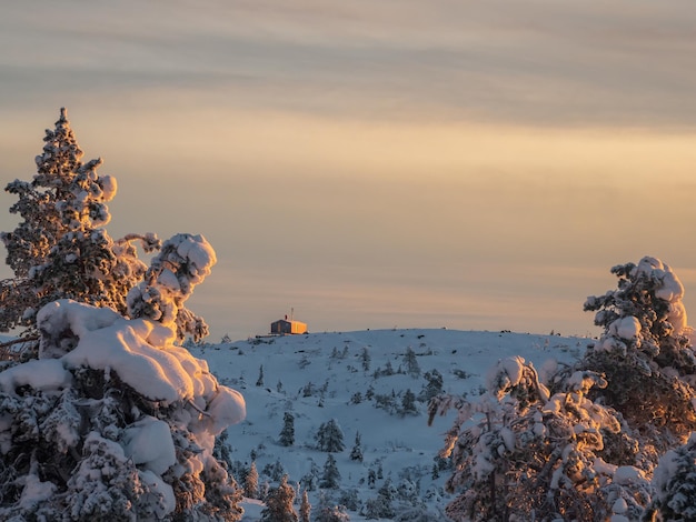 Dawn in the winter snowcapped mountains with a cozy house for tourists Lonely bungalow on a snowy mountain slope under a bright dawn sky