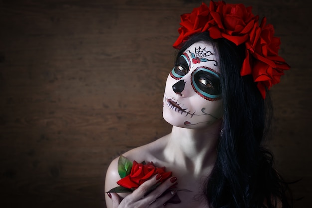 Day of the dead. Halloween. Young woman in day of the dead mask skull face art and rose. Dark background.