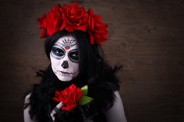 Day of the dead. Halloween. Young woman in day of the dead mask skull face art and rose. Dark background.