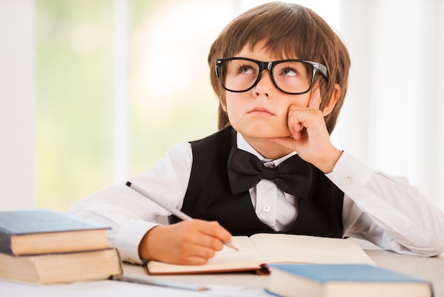 Day dreaming. Bored young boy leaning his face on hand and looking away while sitting at the desk