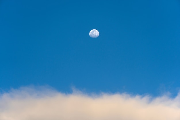 Day moon and strange clouds on the blue sky