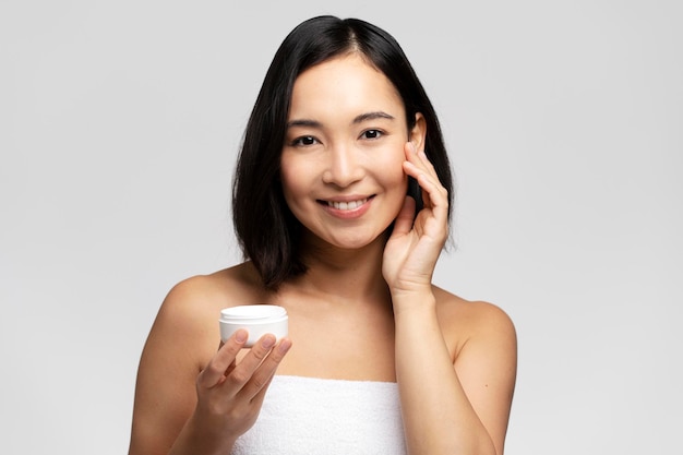 Dazzling young woman applying moisturizing cream on her face