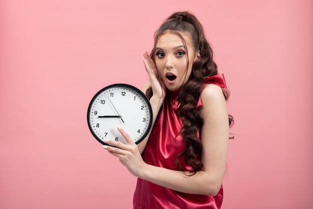 Deadline time has run out woman showing clock poses standing against pink backdrop of studio