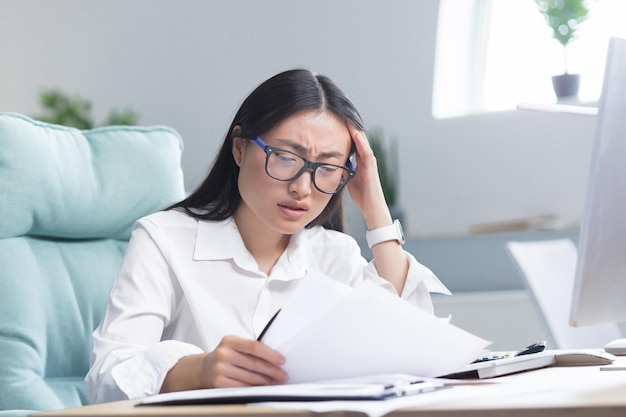 Deadlines are burning young beautiful asian businesswoman is worried sits in the office at the desk