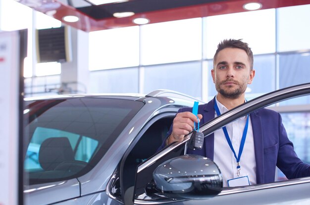 Photo dealer stands near a new car in the showroom