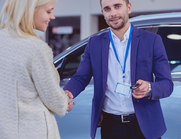 Dealer with woman stands near a new car in the showroom