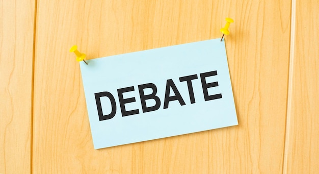 DEBATE sign written on sticky note pinned on wooden wall