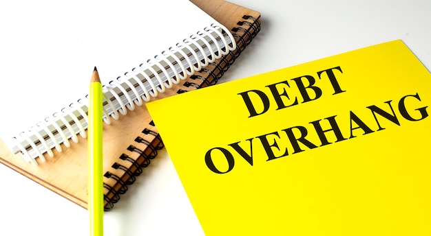 DEBT OVERHANG text on yellow paper with notebooks