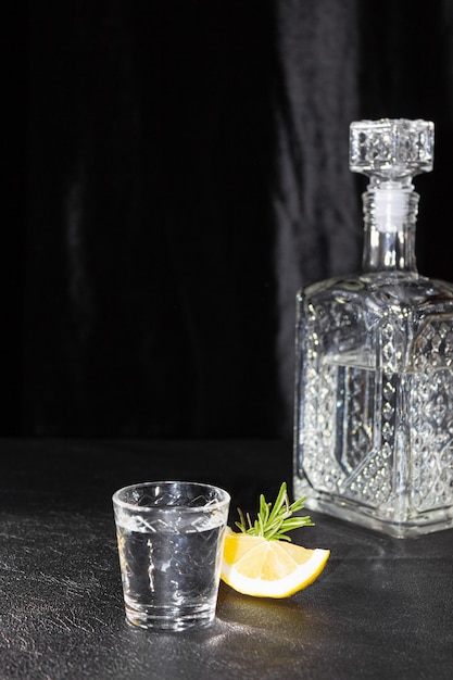 A decanter and a small glass of vodka or other colorless alcoholic beverage on a black background