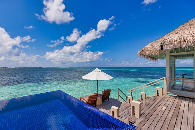 Deck chairs umbrellas at Maldives resort with infinity pool and beach, sea sky view. Luxury terrace