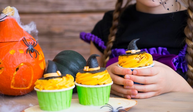 Decor and treats for the holiday. A little girl holding a cupcake in her hands