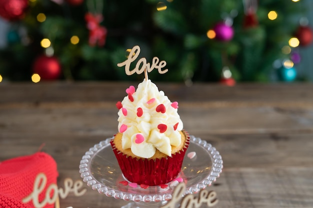 Decorated cupcake in display stand on wooden background with LOVE sign and outoffocus Christmas tree in the background Copy space