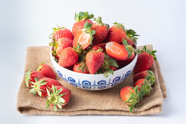 Decorated porcelain bowl filled with strawberries on a sackcloth isolated on a white background