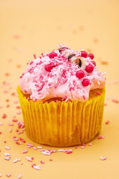 Decorating a Cupcake with Sprinkles on orange pastel background.