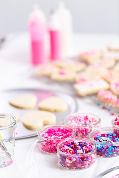 Decorating heart shape sugar cookies with royal icing and pink sprinkles for Valentine's day.