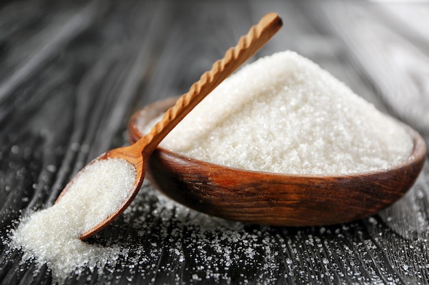 Decorative brown spoon and plate with white granulated sugar on black wooden background