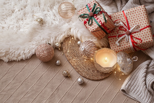 Decorative burning candle on the background of Christmas gifts with cozy things and decor details close up.