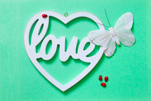 Decorative heart with the word love a butterfly and ladybugs with green background