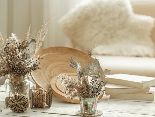 Decorative items in the cozy interior of the room, a vase with dried flowers on light wooden table.