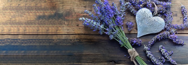 Decorative metal heart among flowers of lavender on wooden background with copy space