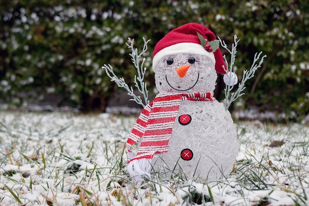 Decorative snowman in red hat and scarf on snow covered lawn. Christmas scenery.