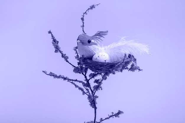 On a decorative tree a nest with eggs and a small yellow bird on a very peri  background close up with copy space