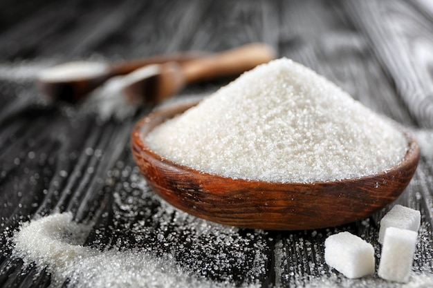 Decorative wooden plate full of sugar on black background