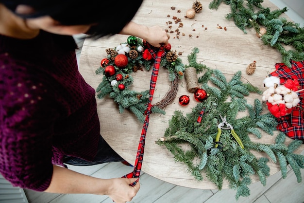 The decorator ties a scottish fabric bow on a christmas decoration made of spruce branches on the de...