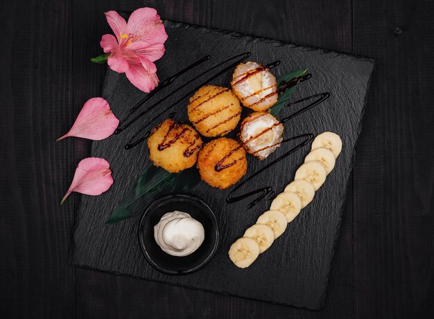 Photo deep fried banana sushi balls being served on black stone platter