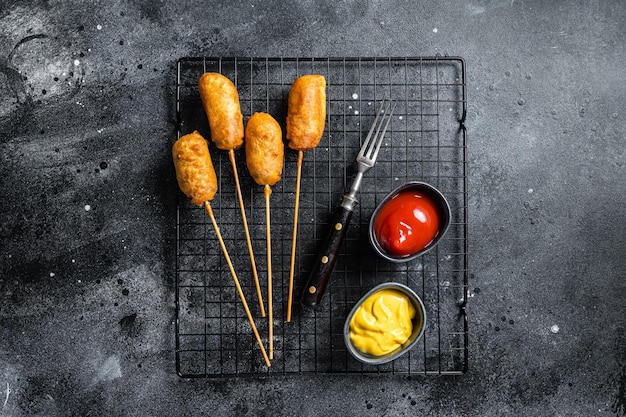 Deep fried corn dogs with mustard and ketchup Black background Top view