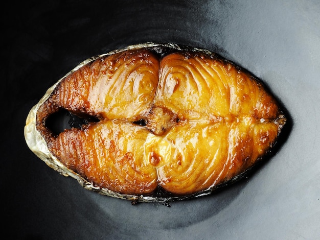 Deep fried piece of sliced mackerel on black dish, fried preserved sun dried fish, fatty food