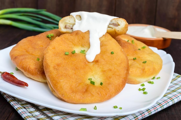 Deep frying pies with meat on a white plate with sour cream on dark wooden background