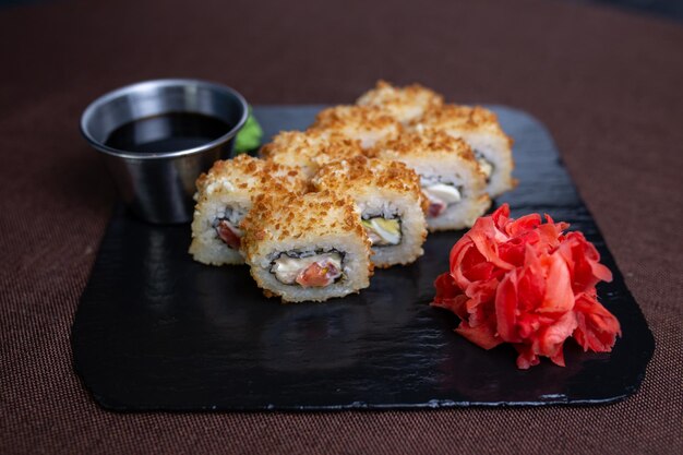 Deepfried sushi roll with soy sauce and wasabi on a black stone plate