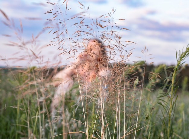 Defocused woman sitting inside summer field with green grass enjoying slow life in nature female in ...