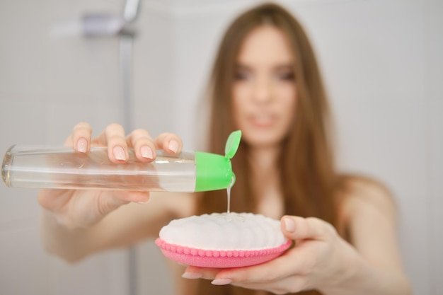 Defocused woman stands in bathroom cabin squeezing refreshing shower gel on a washcloth