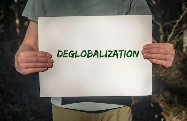 Deglobalization and reverse globalization concept. Word on paper placard in male hands with forest background.