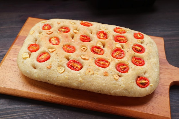 Delectable Freshly Baked Italian Tomato and Garlic Focaccia Bread on Wooden Breadboard