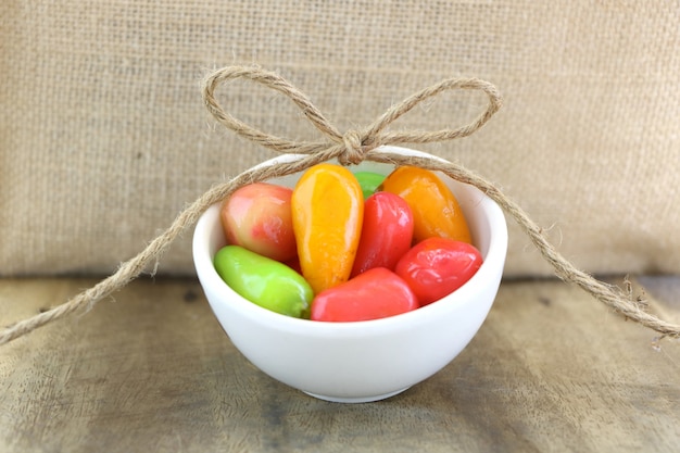 DELETABLE IMITATION FRUITS (KANOM LOOK CHOUP) in white small bowl on wood table and sack background.