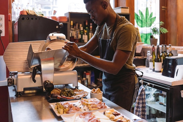 Deli counter worker - cook using slicer - man preparing cold dishes and appetizers