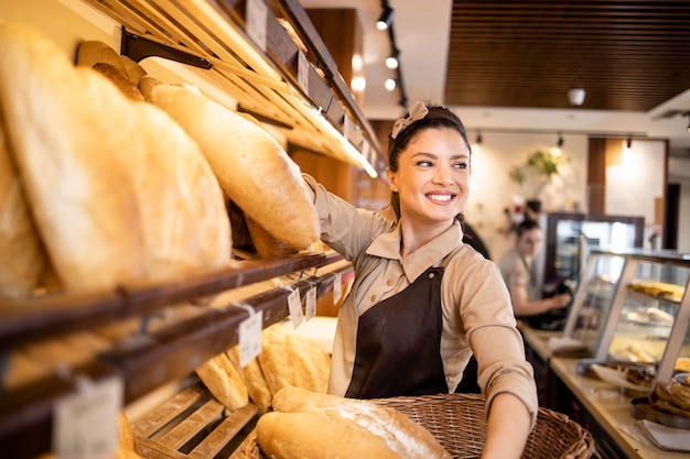 Deli worker arranging fresh pastries and bred in supermarket bakery department