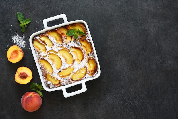 Delicate cake with peaches sprinkled with powdered sugar on a black concrete background