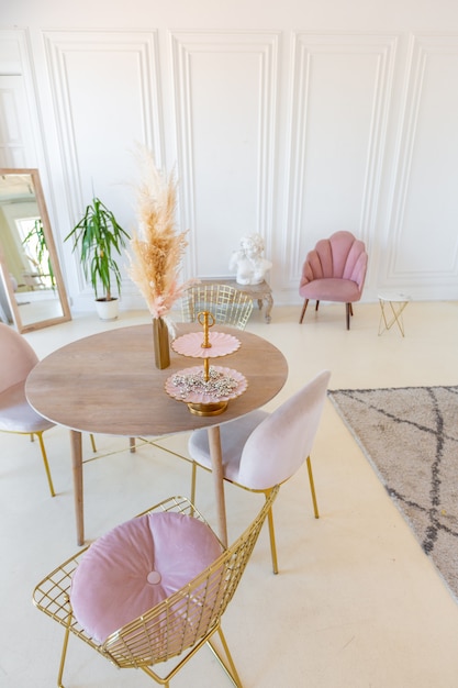 Delicate and cozy light interior of the living room with modern stylish furniture of pastel pink color and white walls with stucco moldings in daylight