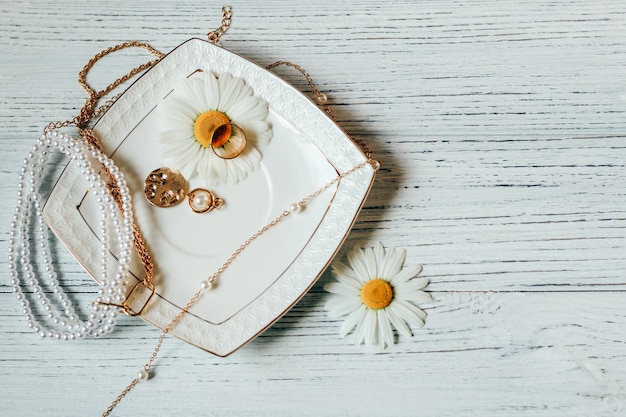 Delicate daisies close-up with gold jewelry. Chains, pendants, rings on a stand.