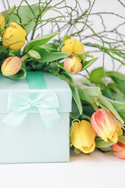 Delicate elegant gift box and a lot of spring yellow tulips on a white background